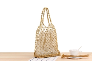 Detail of gold woven mesh beach bag with a cream drawstring pouch on a wooden table