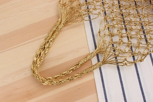 Detail of woven gold handbag featuring a braided handle and metallic mesh texture