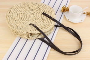 Sac à bandoulière rond en corde de papier tressée avec lanières en cuir sur une table