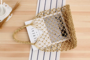 Detailed close-up of handmade gold metallic woven mesh tote bag on a textured wooden table