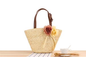 Detail of straw woven beach bag with floral ornaments and brown leather handles