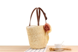 Detail of straw bucket bag with brown PU handle, floral decor, and pearl tassels