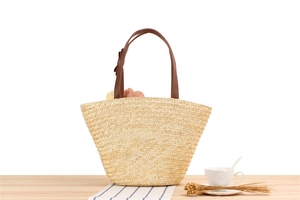 Detailed close-up of handmade straw tote bag with brown leather handles and bow decoration