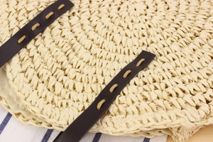 Détail du sac rond en paille montrant le tissage en corde de papier et la sangle en cuir brun