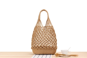 Handmade woven tote bag with open-knit mesh design on a rustic wooden table setup