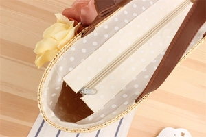 Detail of straw beach bag with floral decor, zipper closure, and polka dot fabric lining