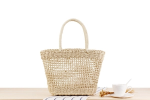 Detail of hollow woven straw handbag featuring round handles on a wooden table setup