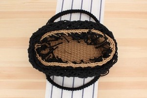 Close-up of a woven tote bag with black rope exterior and fringe detail on wood background