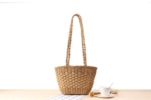 Detail view of straw woven tote bag with wave texture and slim shoulder straps on wood surface