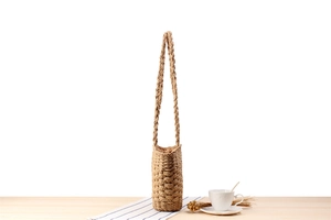 Detail of a cylindrical straw shoulder bag showing textured weave and braided handle