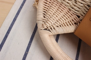 Dettaglio della borsa in paglia intrecciata con manici robusti, patta in pelle e oro