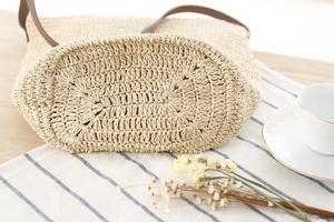 Détail de la base en corde de papier tissée main et des anses en cuir brun du sac beige