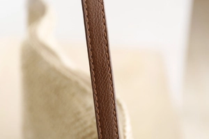 Détail de la couture de la bandoulière en cuir brun sur le sac de plage tissé beige