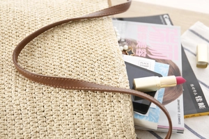 Gros plan du sac bandoulière beige en papier tissé avec bandoulière marron et magazines