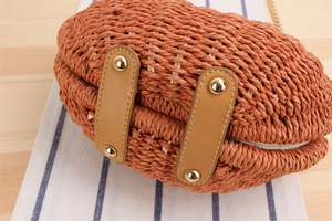 Dettaglio borsa in paglia intrecciata con manici in pelle marrone e rivetti dorati