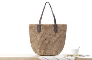 Détail du sac cabas en paille avec poignées en cuir marron sur bois