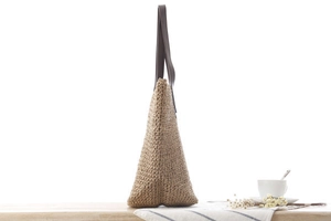 Détail d'un sac de plage tressé en corde de papier avec poignées en simili cuir sur bois