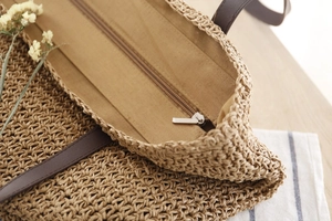 Détails du sac de plage en paille tressée montrant la texture, les anses en cuir et le zip