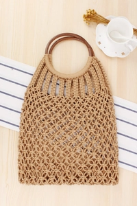 Close-up of beige woven mesh bag with dark round wooden handles on a rustic table