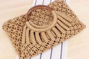 Detail of hand-woven cotton rope beach bag with dark round wooden handle on a wooden table