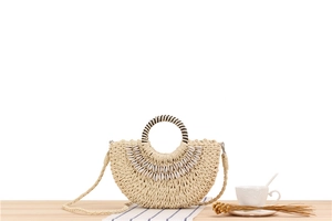 Detail view of a semi-circular straw woven handbag with natural shell decoration on a desk