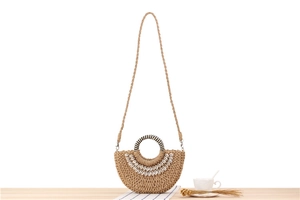 Detail of a semi-circular straw bag featuring natural shell accents and a woven handle