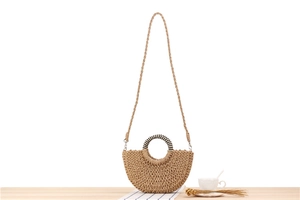 Detail of semi-circular straw woven handbag with shell decor on a wooden table
