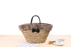 Detail of hand-woven straw bag featuring plush fur trim and a delicate black bow decoration