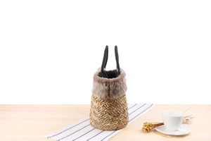 Detail of woven straw bucket bag with grey faux fur trim and black rope handles