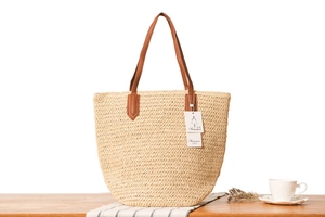 Gros plan du sac fourre-tout en paille tissée avec anses en cuir marron sur bois