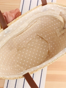 Handmade straw tote bag with pink floral accents and brown leather handles on wooden desk