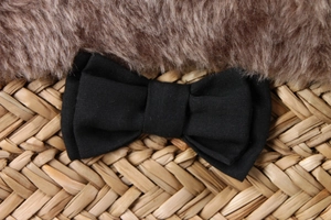 Detail of a black fabric bow accessory on a woven straw and plush texture background