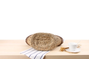 Macro shot of the oval woven base of this brown straw bag on a light wooden table