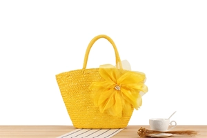 Detail of yellow woven straw bag featuring a large organza flower on a wooden table