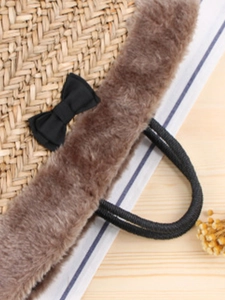 Straw beach tote with brown faux fur trim and a black satin bow on a wooden surface