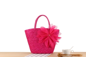 Macro detail of hand-woven magenta straw tote bag with oversized silk flower and pearl