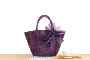 Detail of a purple woven straw bag featuring a large translucent silk flower ornament
