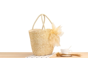 Detail of hand-woven straw tote bag with large decorative fabric flower on light wood surface