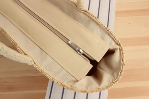 Close-up detail of smooth zipper closure and beige fabric lining on woven straw beach bag