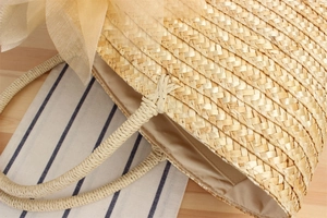 Detail of hand-woven straw bag featuring delicate mesh bow and sturdy braided handles