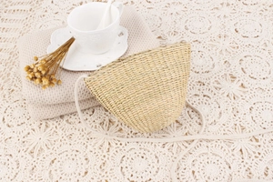 Gros plan d'un sac bandoulière en paille tressé main sur une nappe en dentelle blanche