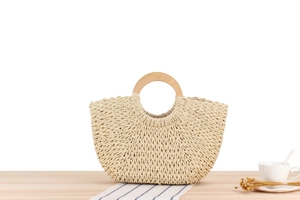 Close-up of beige woven paper rope bag with circular wooden handle on a rustic table