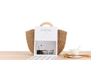 Detail of woven straw handbag with wooden handles on a rustic table with magazine and tea