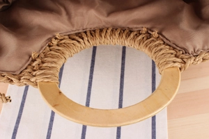 Detail of hand-woven paper rope bag with smooth round wooden handle and fabric lining
