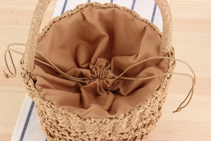 Top view of woven straw bucket bag with dark brown drawstring liner and textured handles
