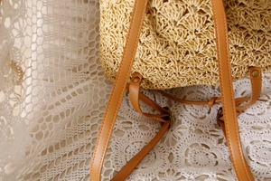 Detail of woven straw backpack with brown leather straps and vintage metal rivets
