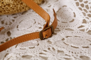 Detail showing the brown leather shoulder strap with a vintage bronze metal buckle on a woven bag