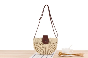 Detail of beige straw crossbody bag with brown leather strap on wooden table decor