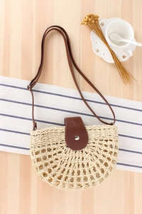 Detail of the hollow handwoven straw bag with dark brown leather strap and metal clasp