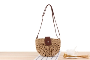Close-up of beige woven crescent beach bag with brown leather flap and hollow-out mesh detail